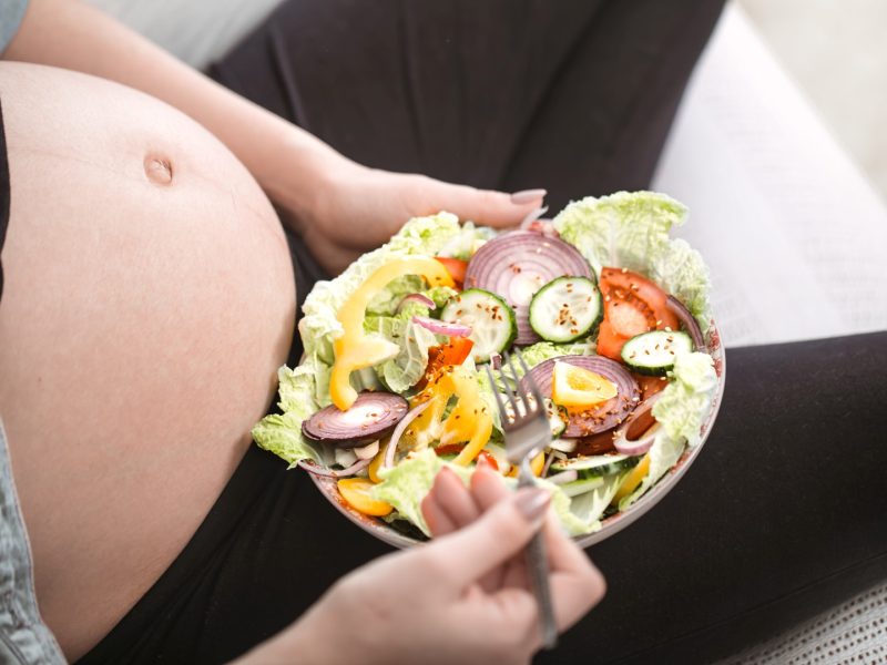 Young pregnant woman eating vegetable salad at home, concept of pregnancy and healthy eating.